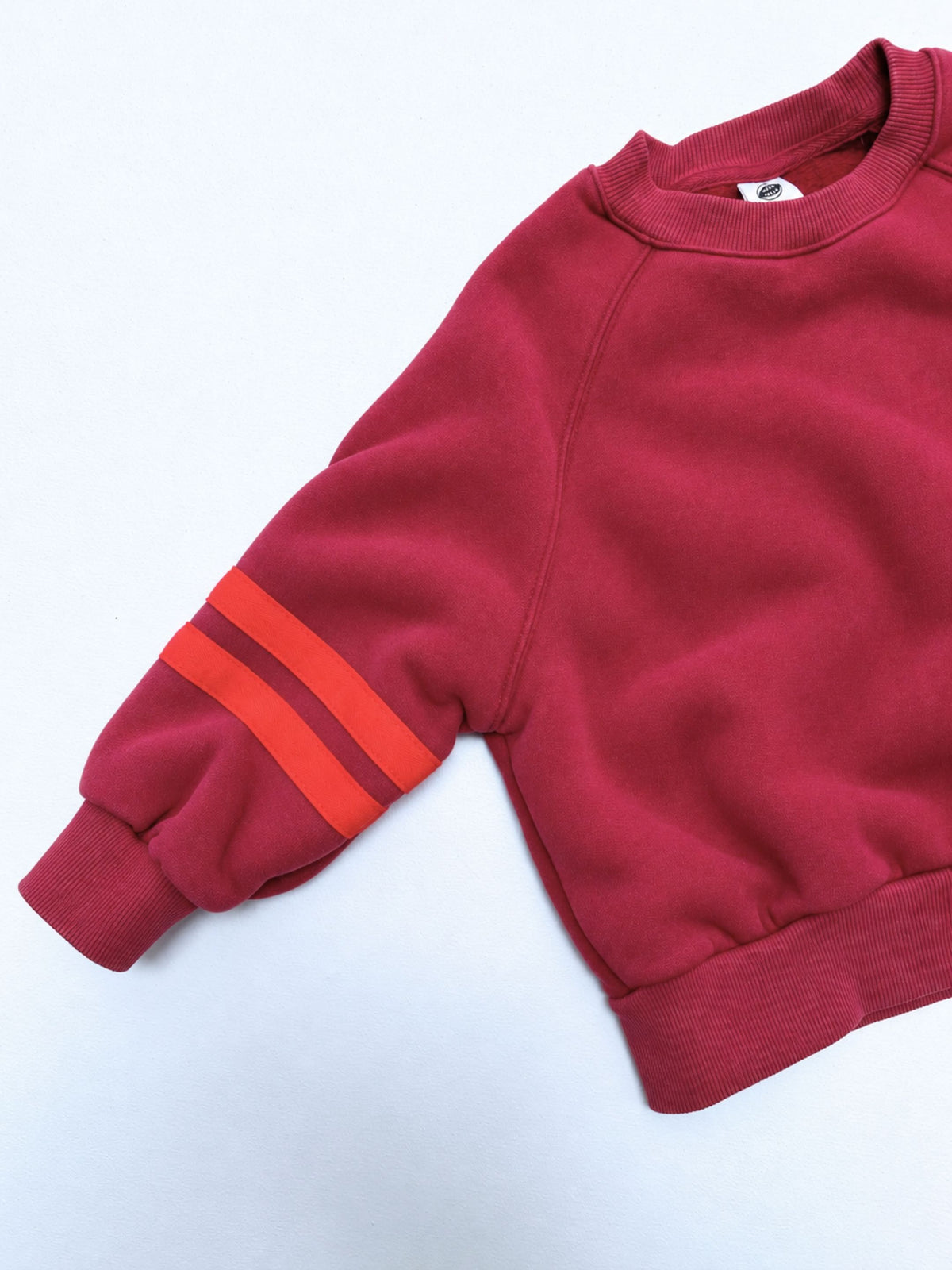 Red | Detail view of kids crewneck sweatshirt in red with two bright red-orange stripes on each sleeve