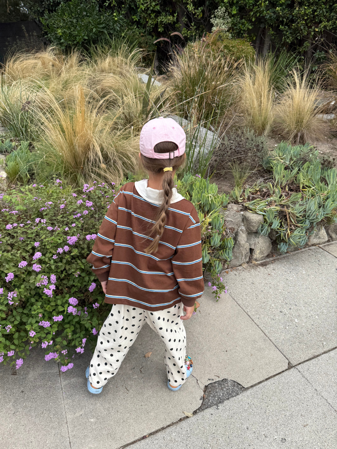 Child walking on a sidewalk with garden and plants in the background