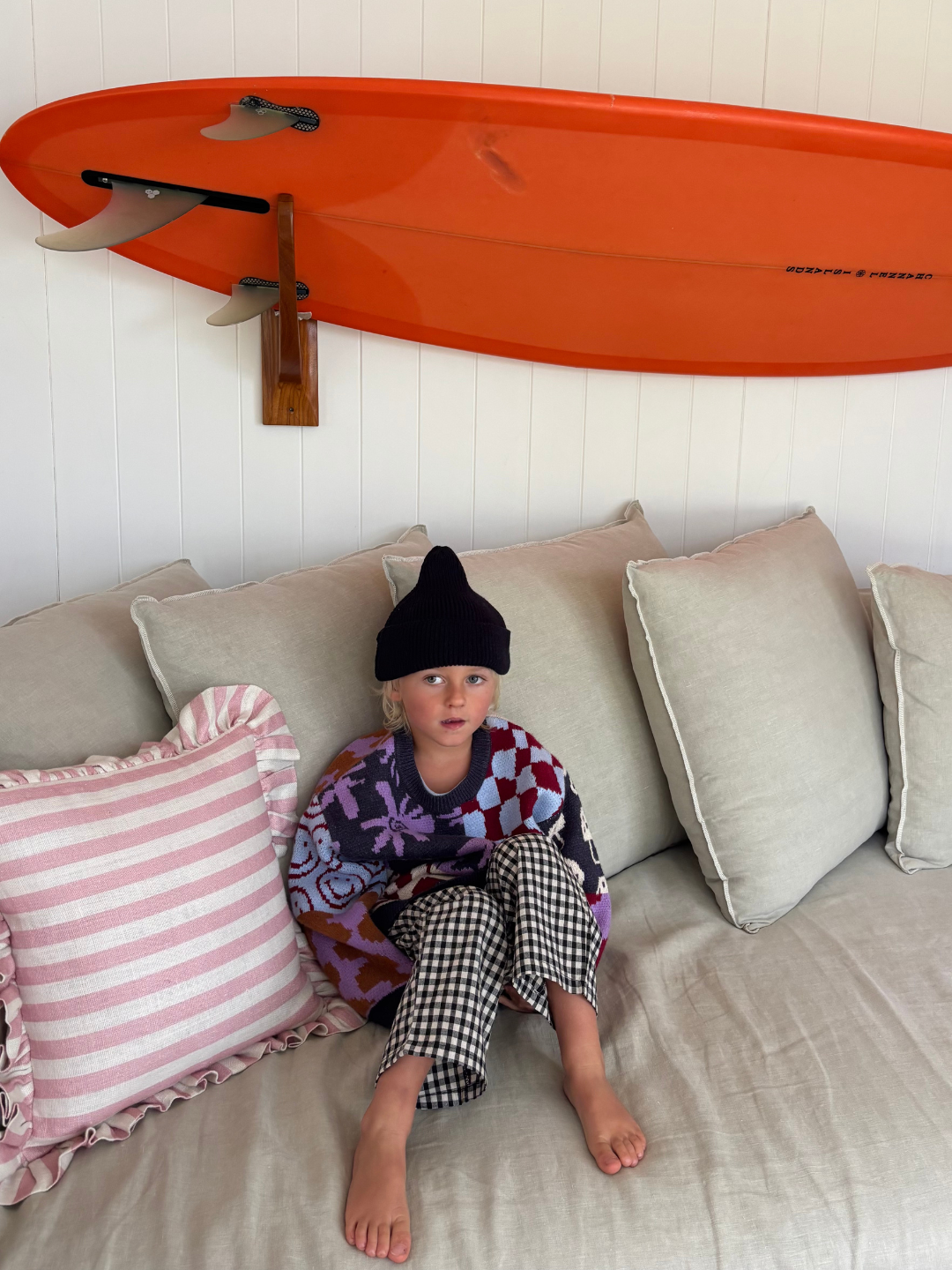 Child sitting on a couch with an orange surfboard above