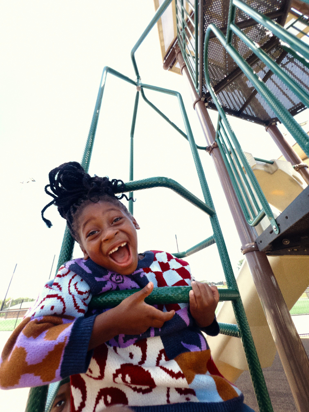 Child playing on a playground structure with a colorful sweater