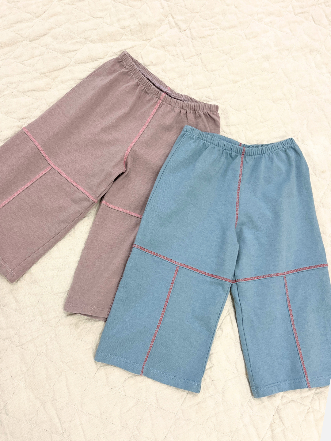Lavender/Pink and Blue/Red Contrast Stitch Baby Pants laid on the ground next to each other.