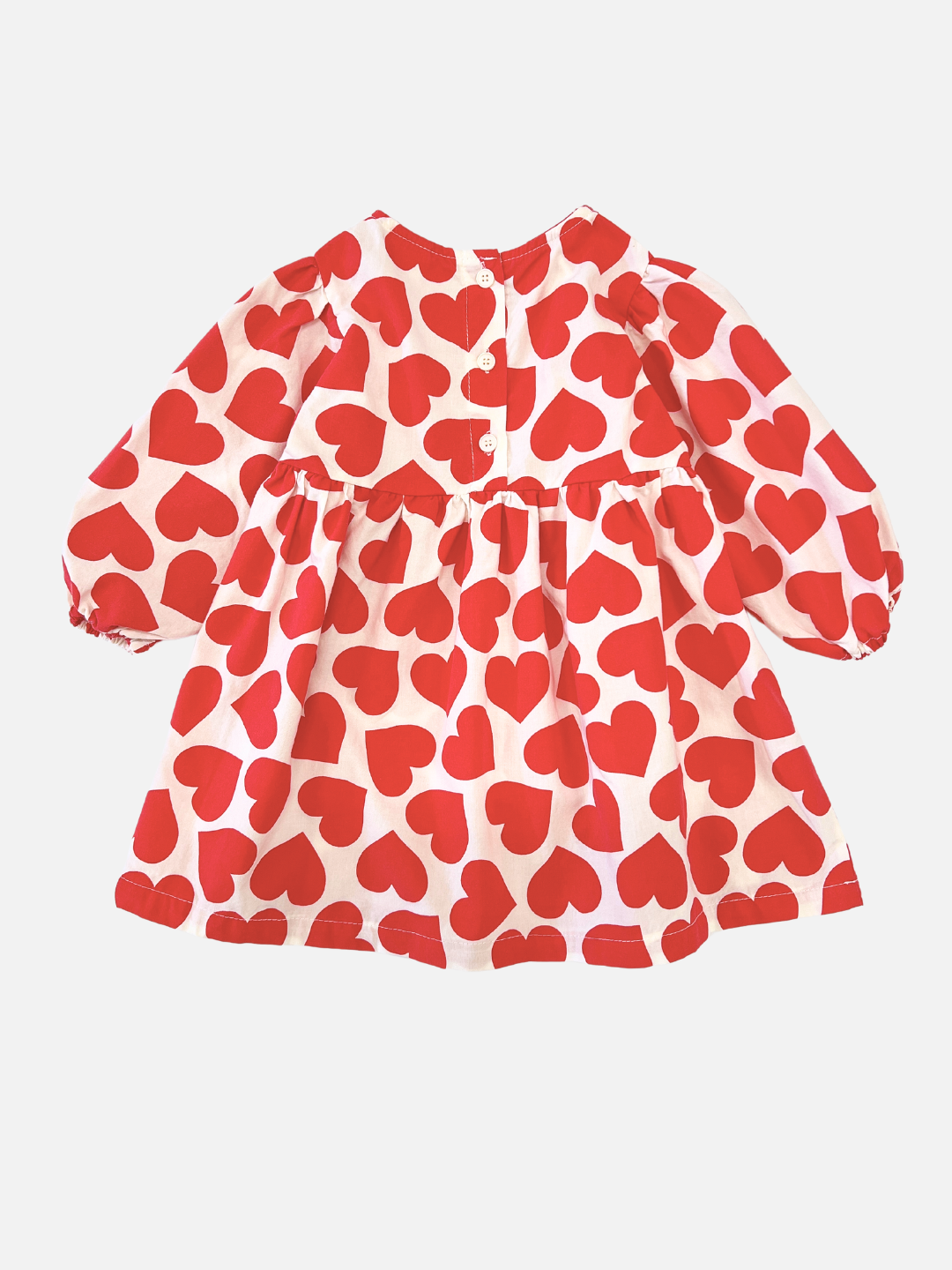 back view of kids dress in white with red hearts printed closely all over, showing three buttons in back, and with a round neck, high waist, long puffed sleeves and a loose, voluminous shape.