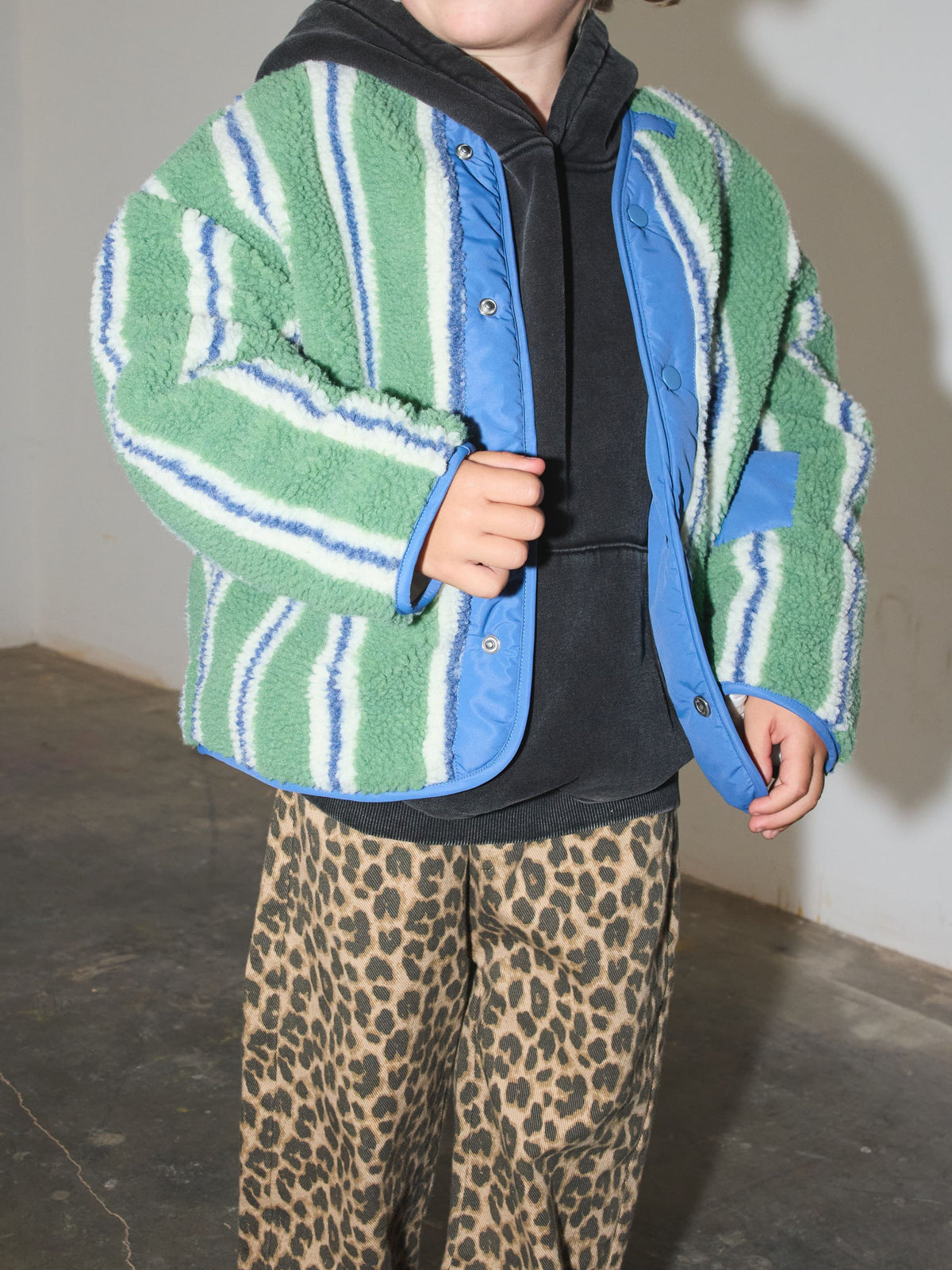 Close-up of the open sherpa jacket with its blue snap placket and blue trim, worn over a charcoal hoodie.