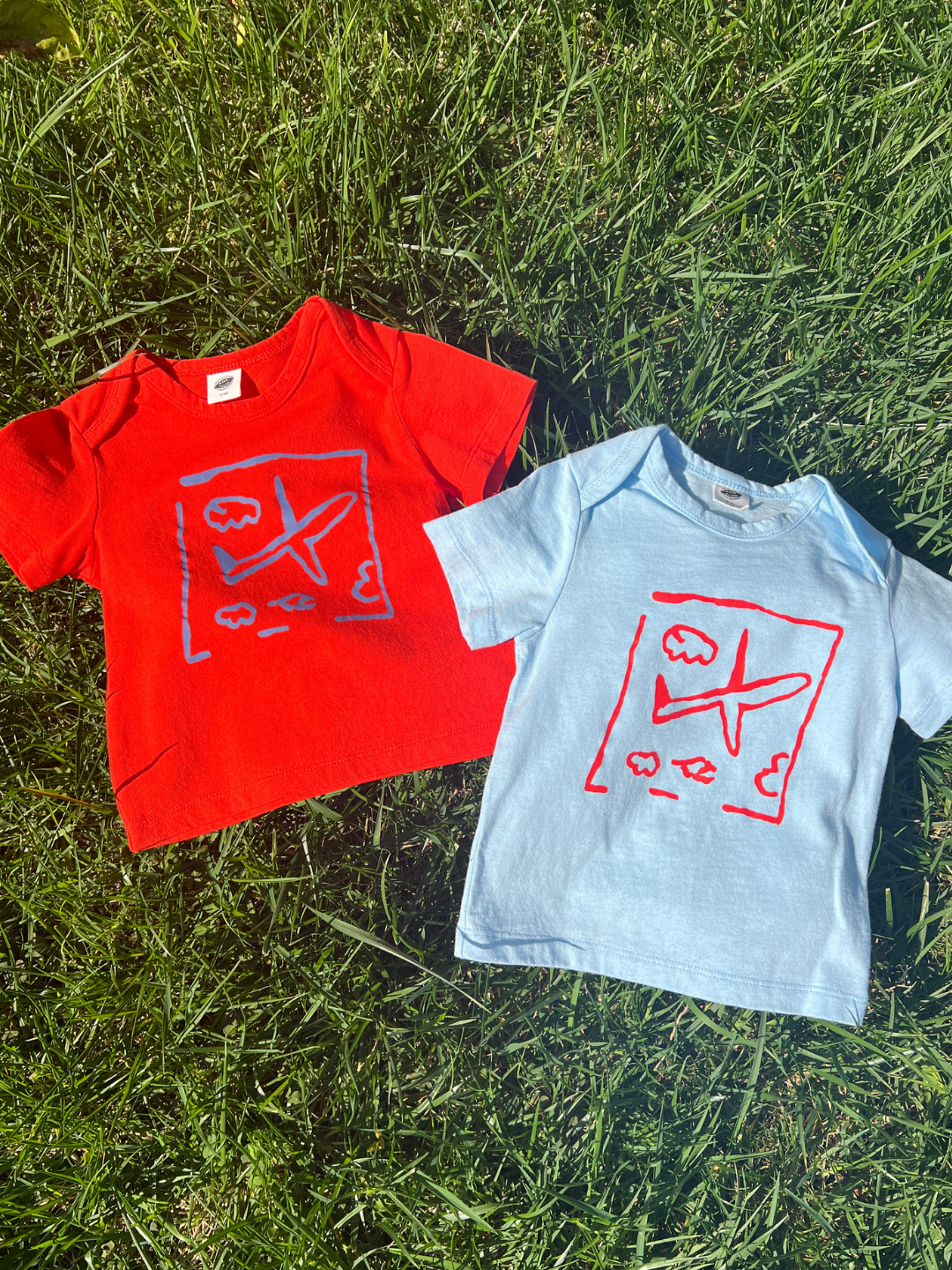 Red and light blue t-shirts with graphic designs on a grassy background
