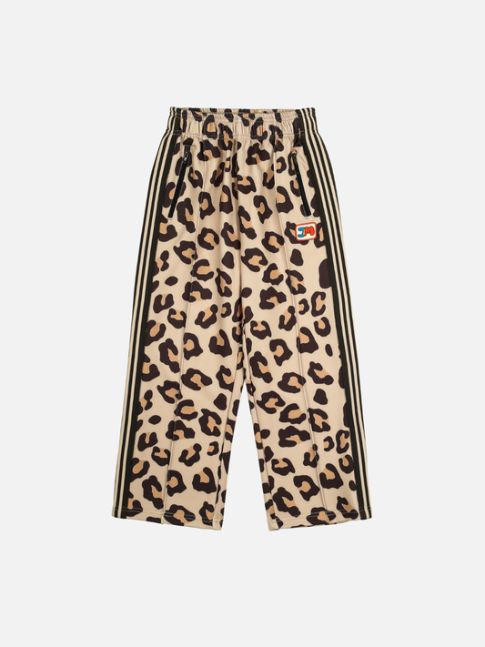 Image of The LEOPARD TRACK PANTS feature leopard print with black side stripes, an elastic waistband, and a small colorful patch on the front. Perfect for stylish casual wear and easy to care for.