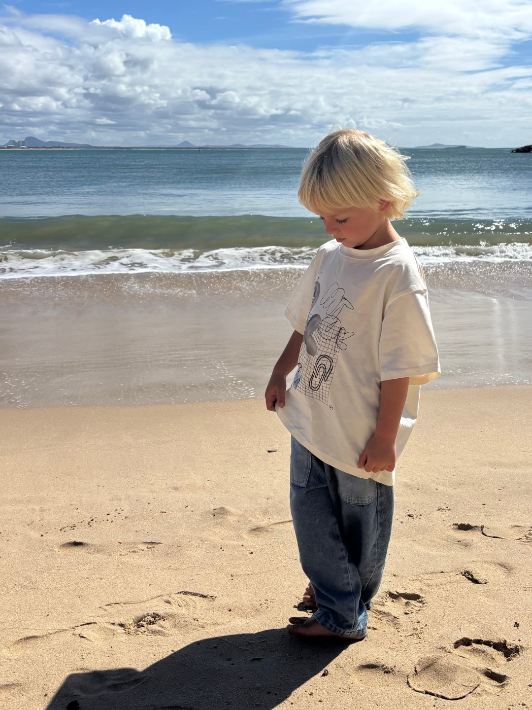 Child standing on a sandy beach with ocean waves in the background