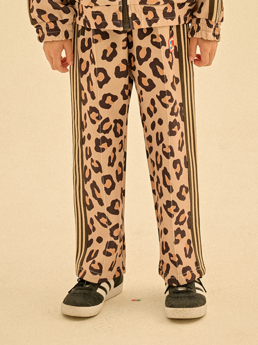 Second image of The LEOPARD TRACK PANTS feature leopard print with black side stripes, an elastic waistband, and a small colorful patch on the front. Perfect for stylish casual wear and easy to care for.