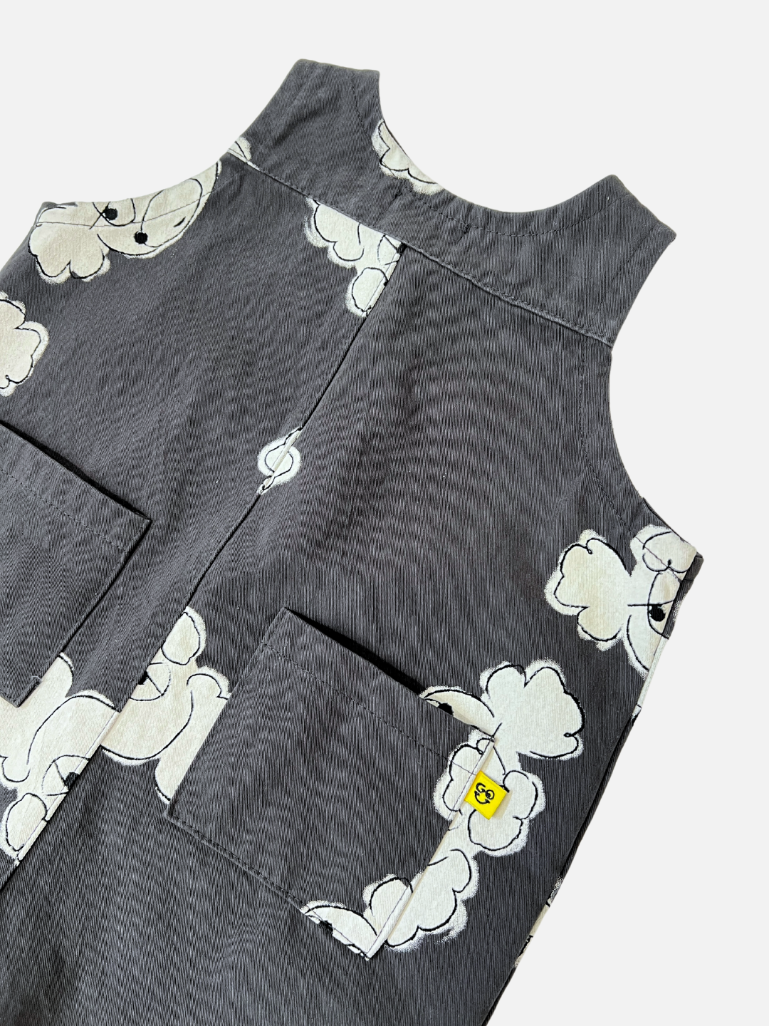 The POODLE OVERALL is a gray apron with poodle doodle and white cloud prints, featuring two front pockets. A small yellow tag from a trendy Korean kids label is attached to one pocket, blending style and practicality seamlessly.