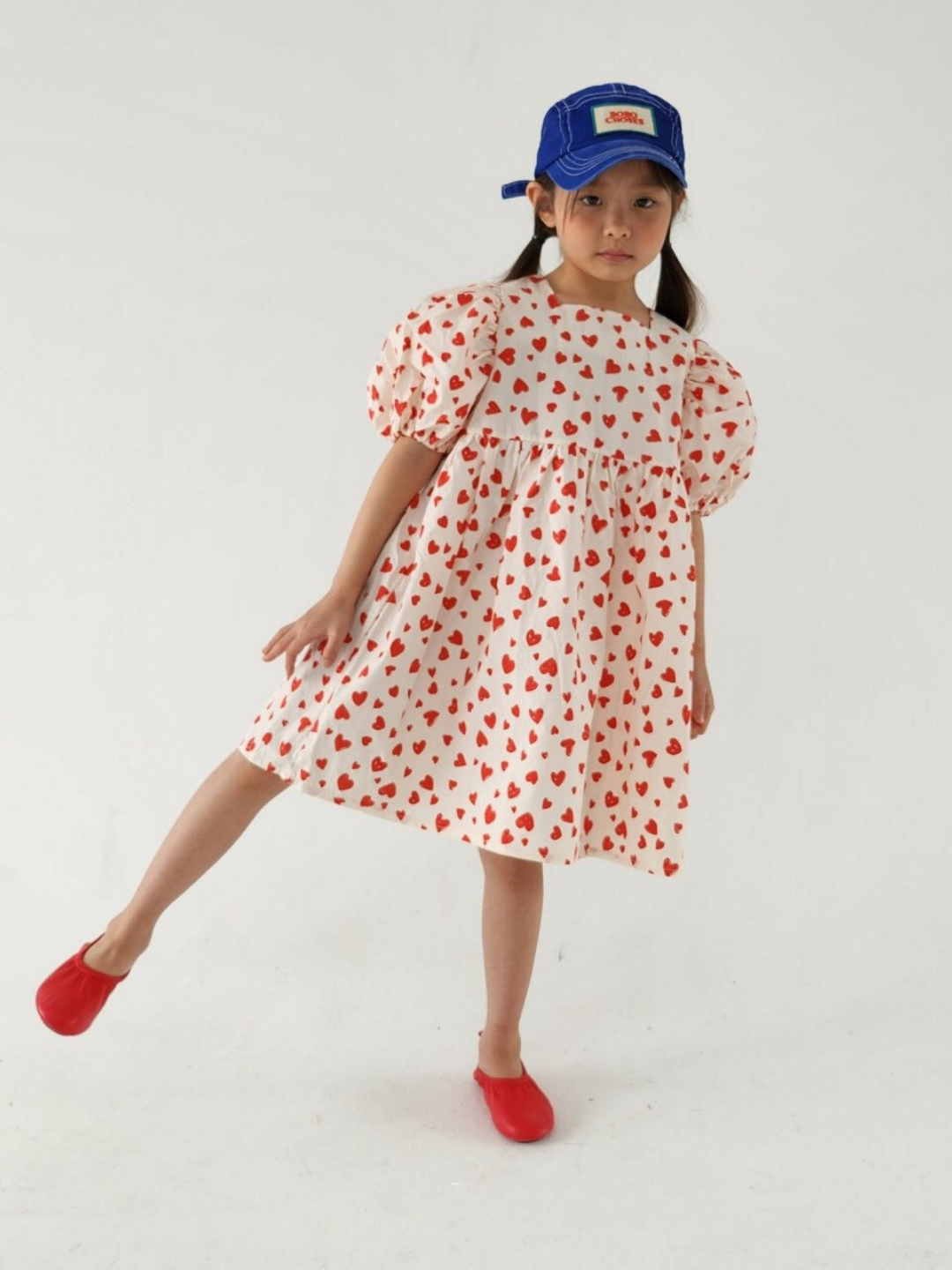 A child wearing a kid's puff-sleeved dress with red hearts on a white background