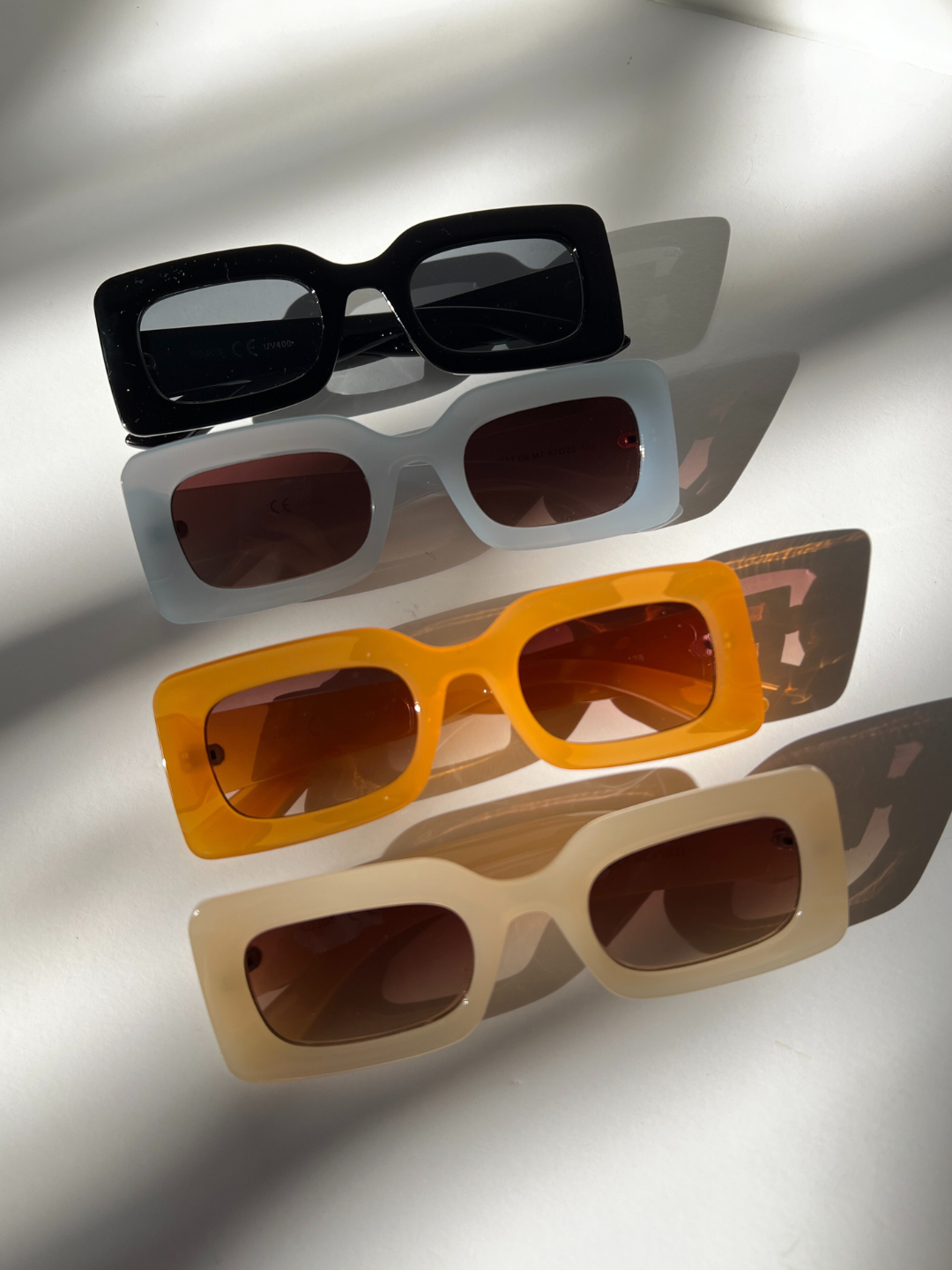 Group of kids rectangle sunglasses in black, blue, orange and cream, lined up diagonally on a white background.