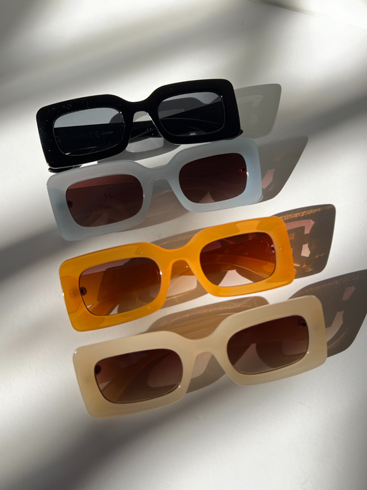 Image of Black | Group of kids rectangle sunglasses in black, blue, orange and cream, lined up diagonally on a white background.
