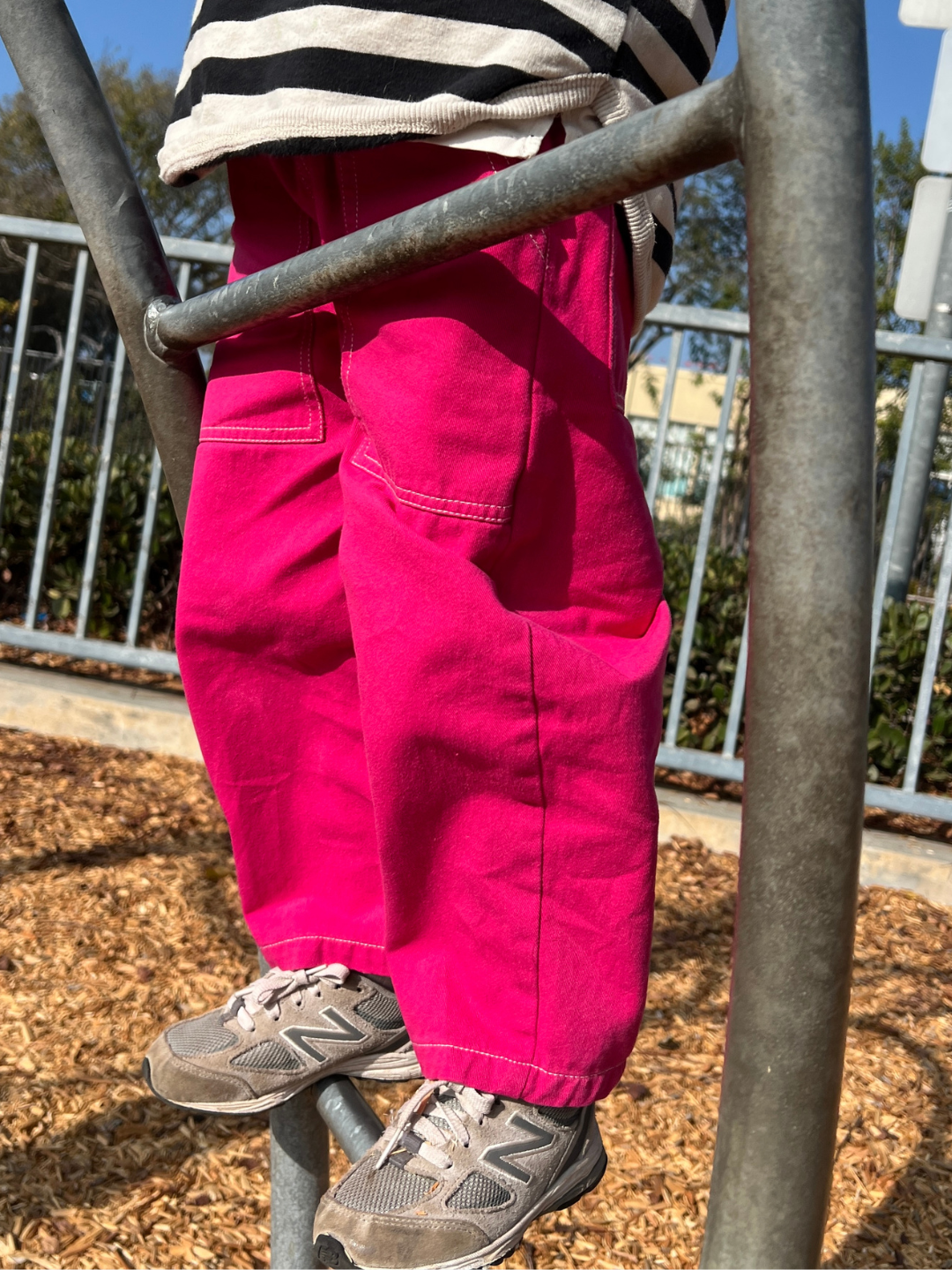 Child wearing pink pants and a striped shirt on playground equipment