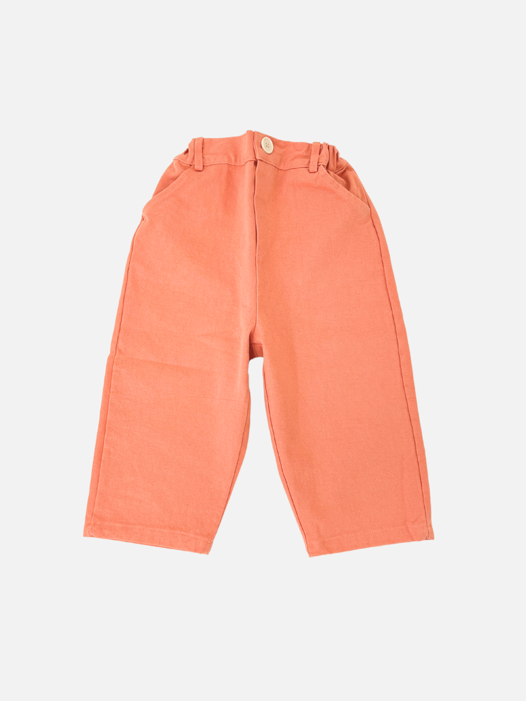 Melon | Melon-colored Tomboy Pants are wide-legged and slouchy with an elastic waistband and button closure, made from cotton twill. These stylish essentials, from a contemporary Korean kids brand, are laid flat on a white background.