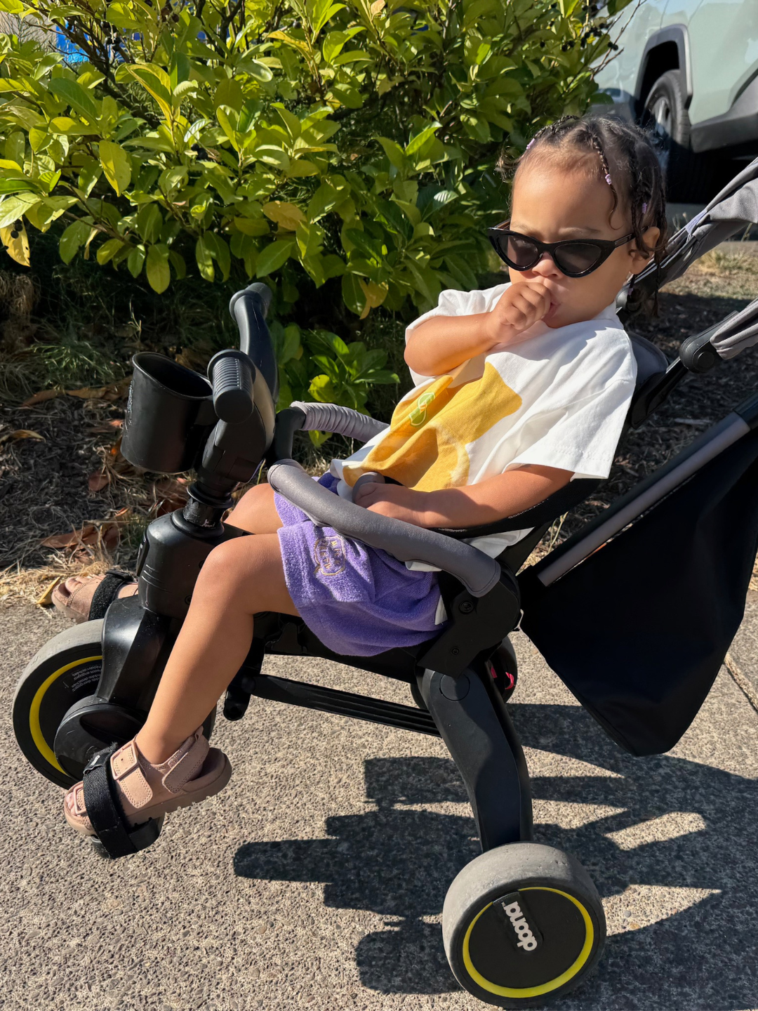 Child sitting in a tricycle outdoors with sunglasses on