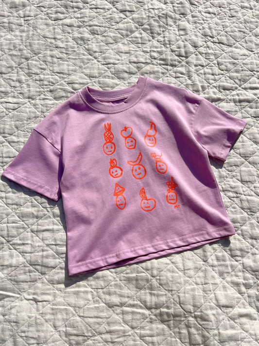 Second image of Violet | A front view of the kids' Fruit Face tee in Violet. Printed faces are wearing fruit hats, all in orange color. 