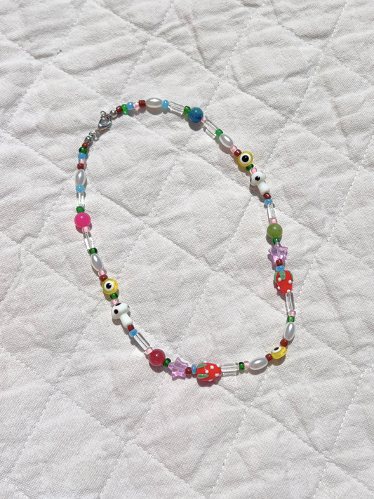 Image of The GAIA NECKLACE, accented with vintage glass beads in assorted shapes and vibrant colors, is displayed on a white quilted fabric background.