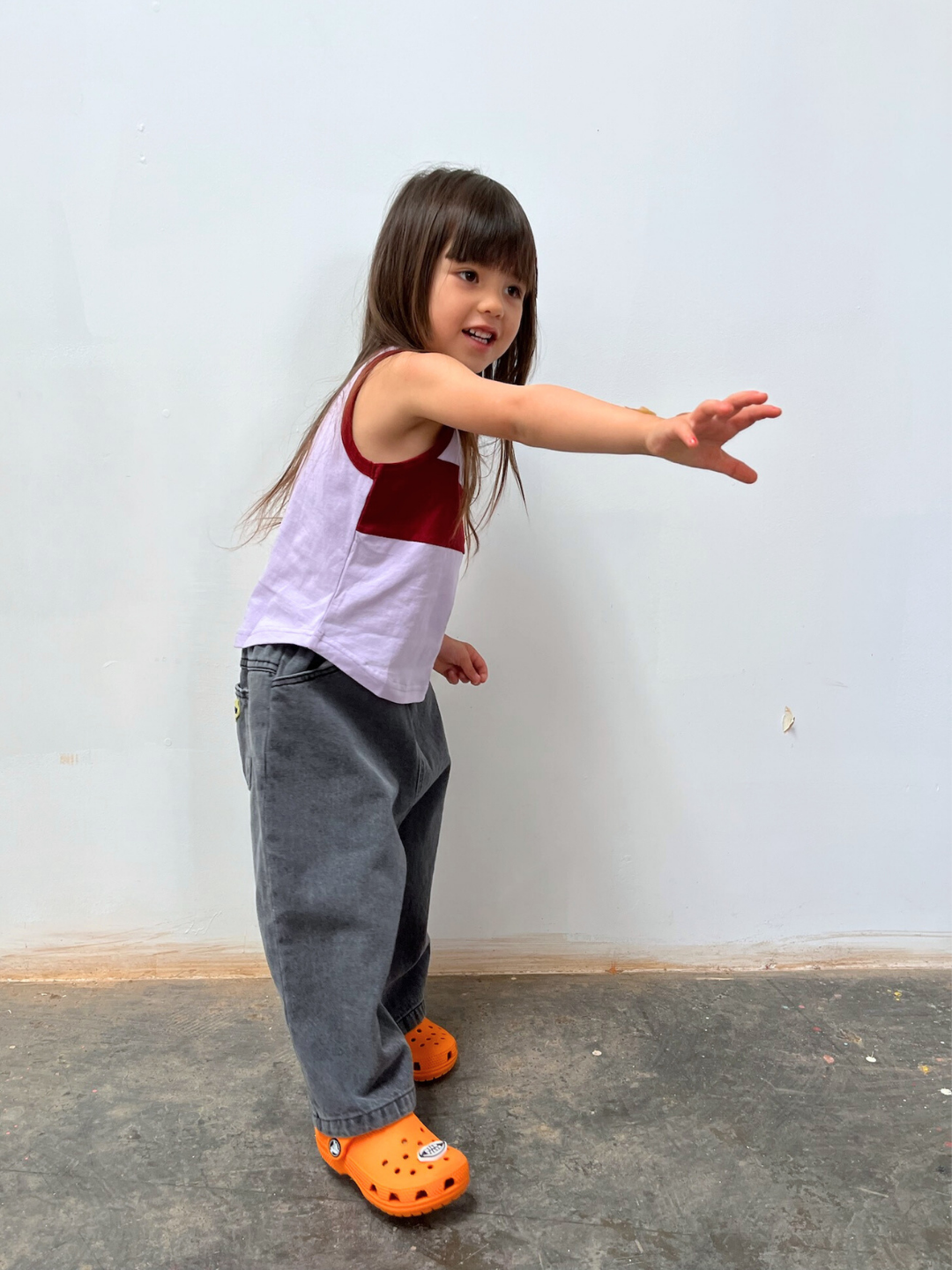 Purple/Maroon | A young child wears the TRACK TANK, gray pants, and orange shoes while standing on a concrete floor and reaching out with one arm against a plain light wall, highlighting the relaxed fit and vintage sportswear vibes of the top.