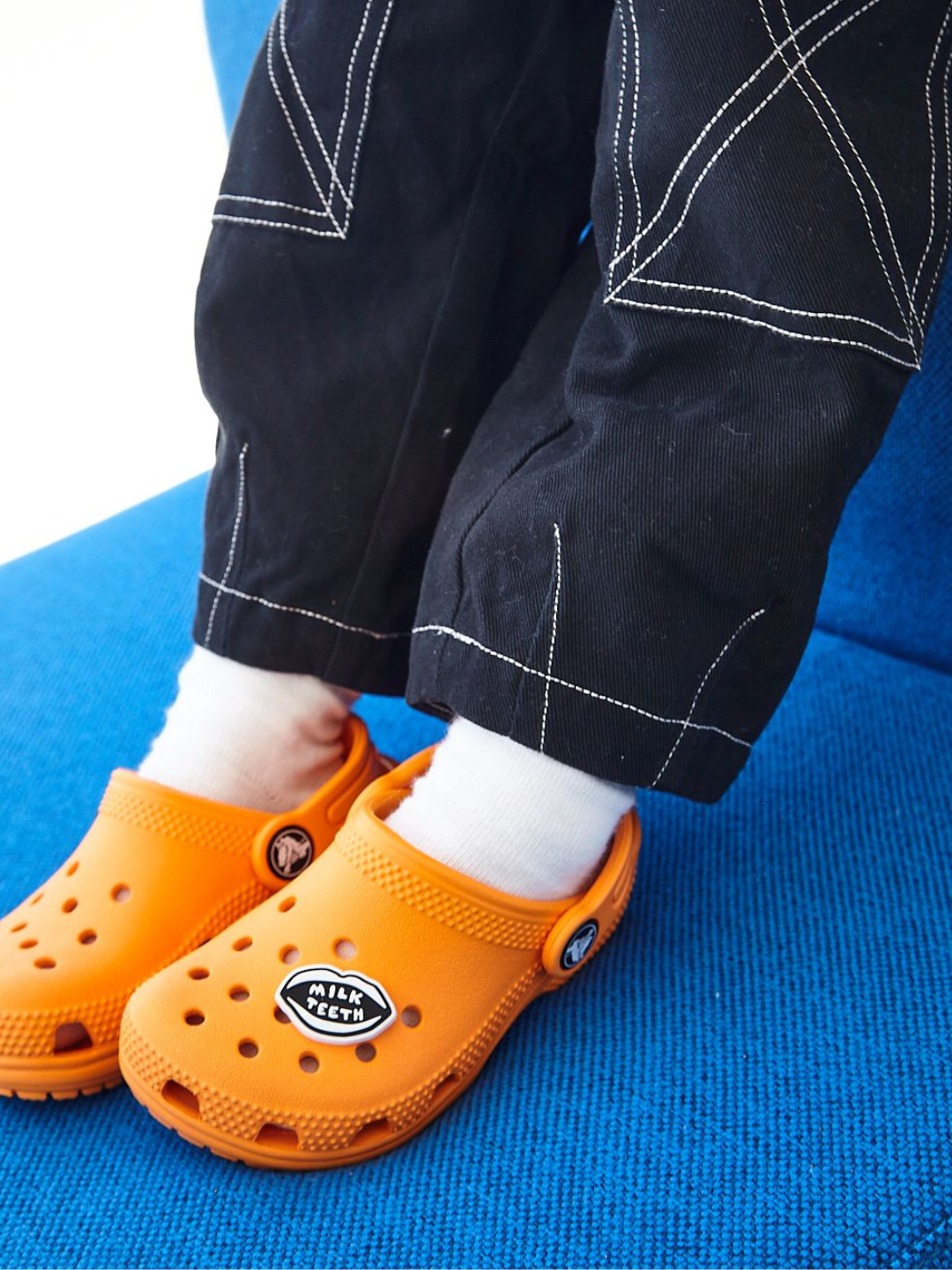 A child wearing a pair of orange Crocs with a Milk Teeth logo charm