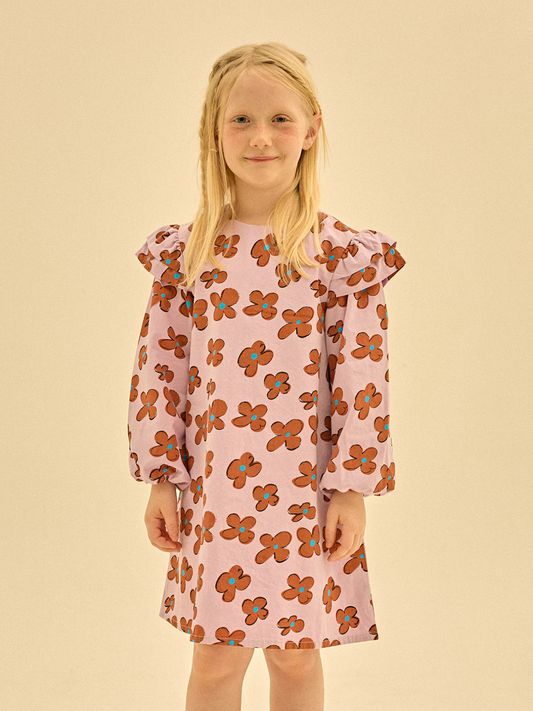 Second image of The FLOWER FRILL DRESS, a long-sleeved children's dress with a light purple background adorned with an orange and red floral pattern and charming ruffled shoulders, is perfect for showcasing in your merchandising lineup.