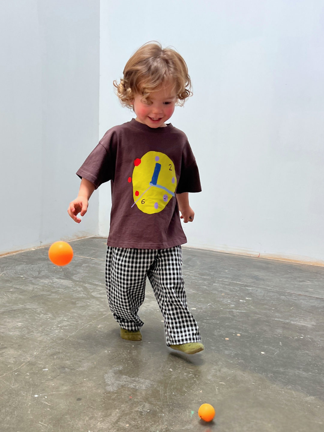 Child playing with balls on a concrete floor against a light blue wall