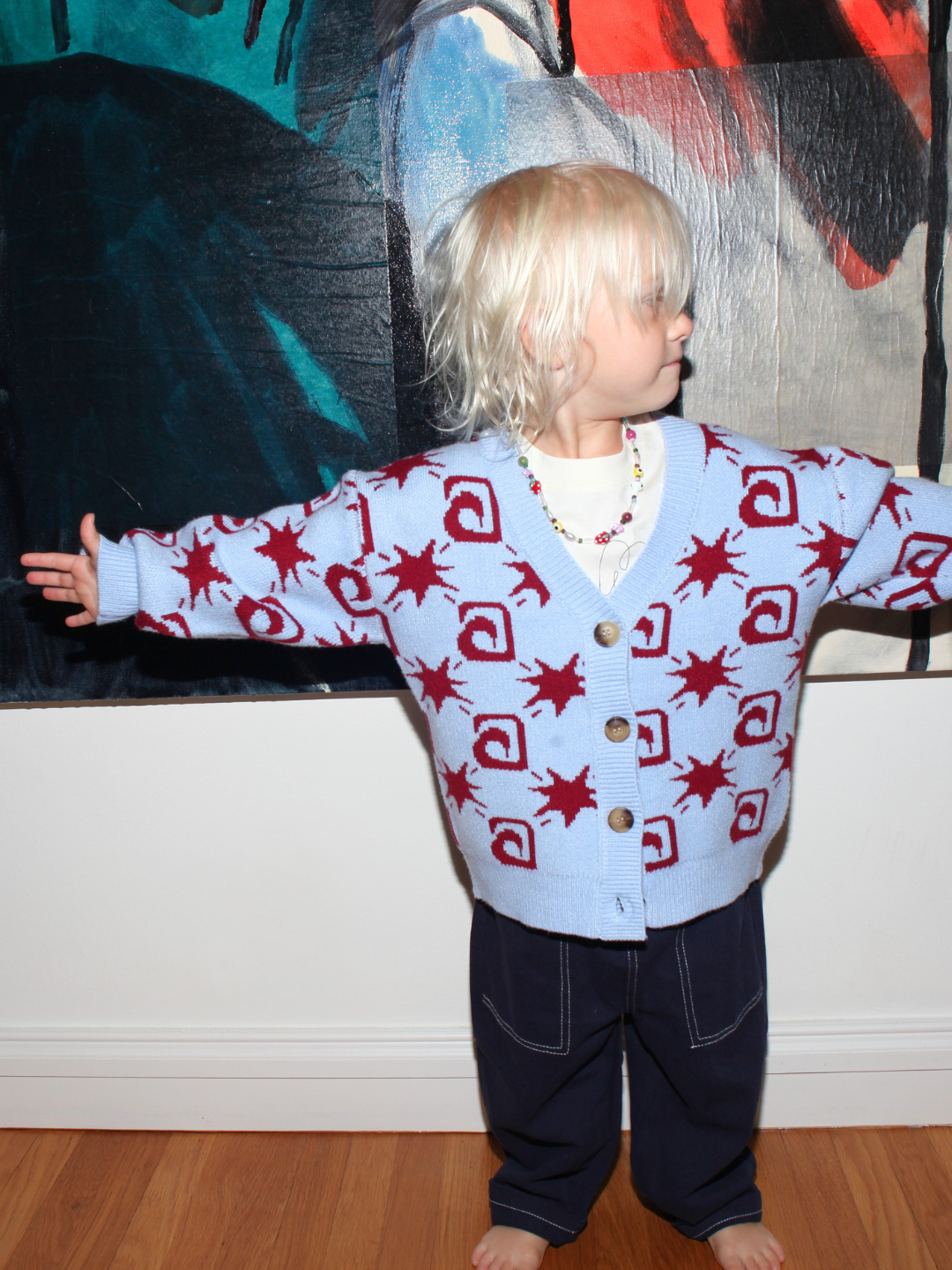 Child wearing a patterned cardigan in front of a colorful abstract painting