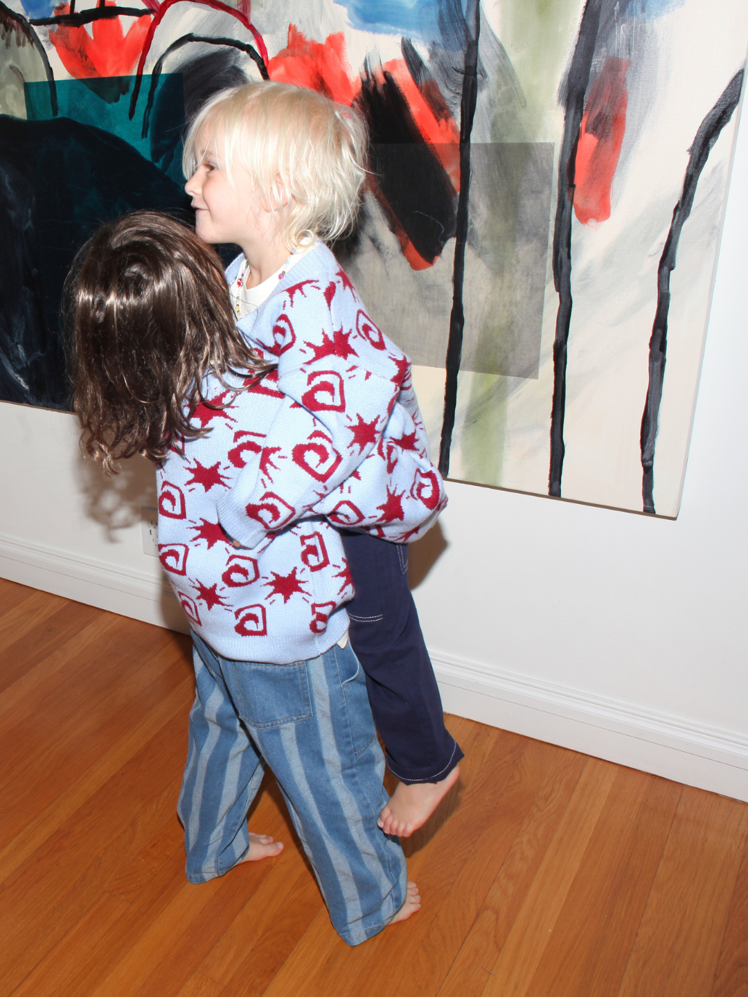 Sky | Two children standing on a wooden floor with abstract art in the background