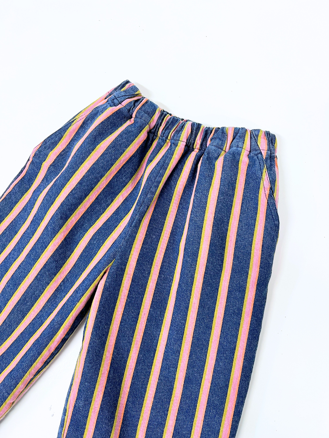 The EVER DENIM WIDE LEG STRIPED TROUSERS feature vertical pink, yellow, and green stripes on blue denim with an elastic waistband. Displayed on a white surface, these unisex pants embrace a minimalist aesthetic for versatile style.