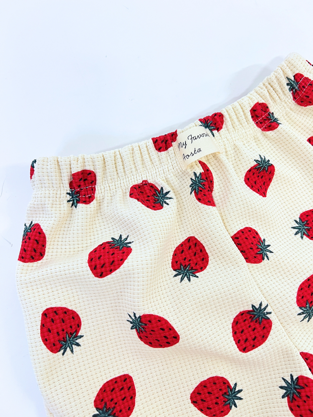 Strawberry Waffle Shorts crafted from textured fabric feature an elastic waistband and a small label adorned with a strawberry pattern.