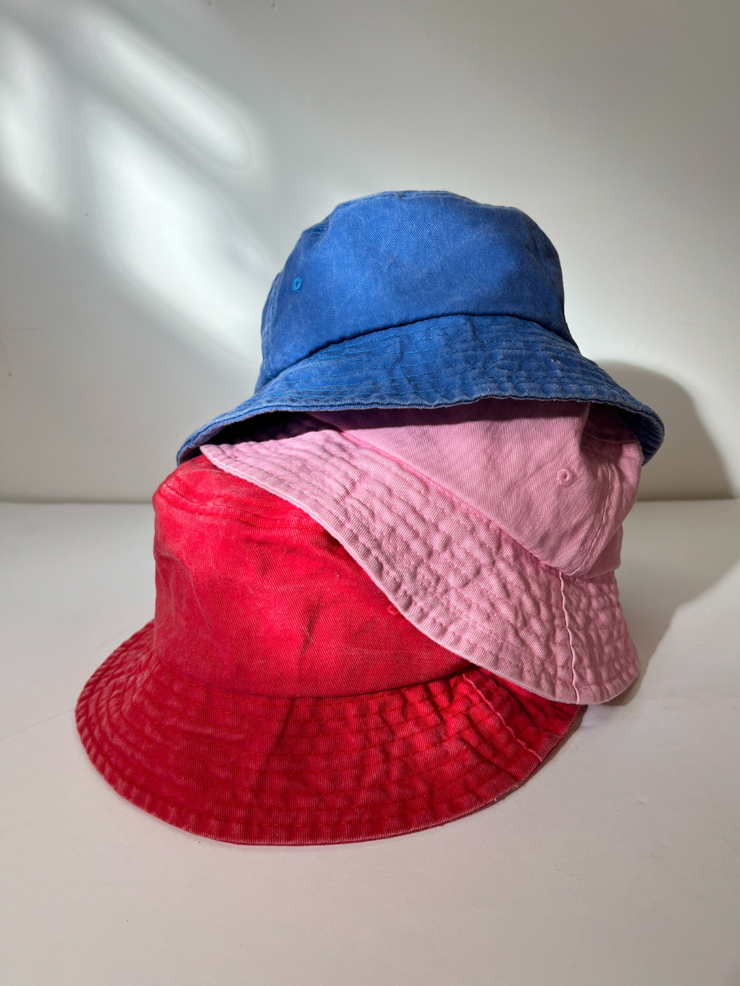 Blue | A trio of PIGMENT BUCKET HATs in blue, pink, and red rests against a plain backdrop, adding vintage flair to any outfit.