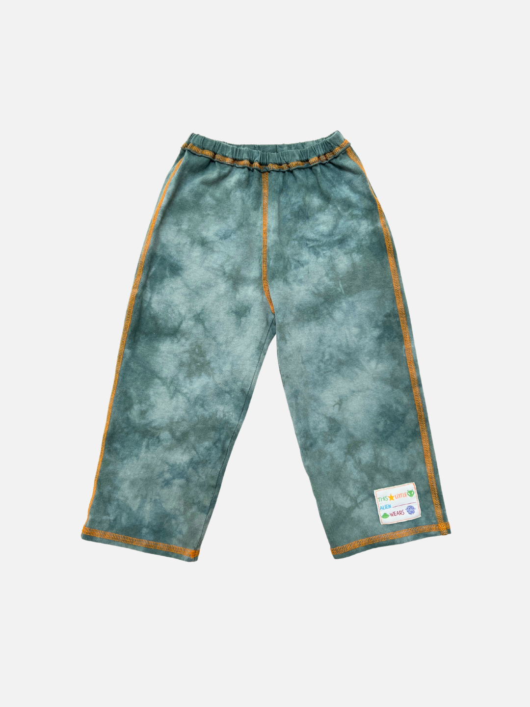 Loose-fitting sage COSMO TIE DYE PANT made of cotton jersey with orange stitching, elastic waistband, and a small rectangular patch near the left ankle, displayed on a white background.