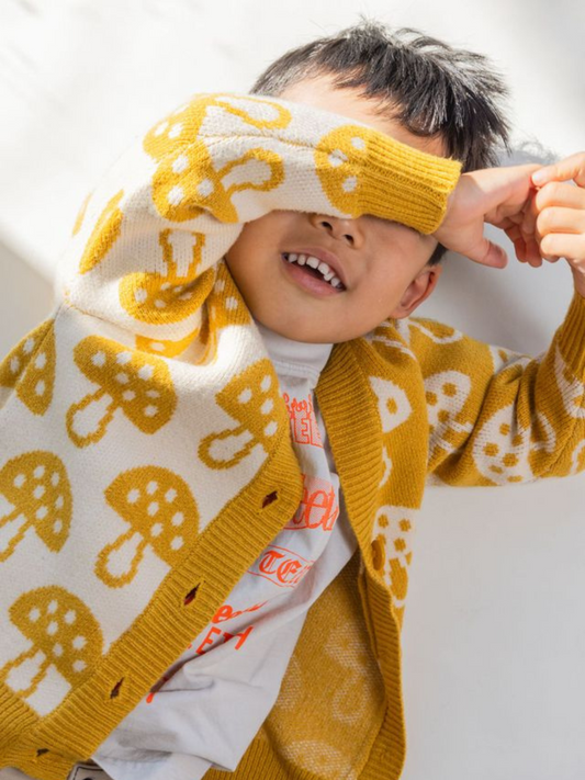 Second image of The SHROOM CARDIGAN, a mustard yellow cardigan adorned with beige mushroom patterns, featuring a V-neck and three buttons down the front, is perfectly described in detail for clarity.