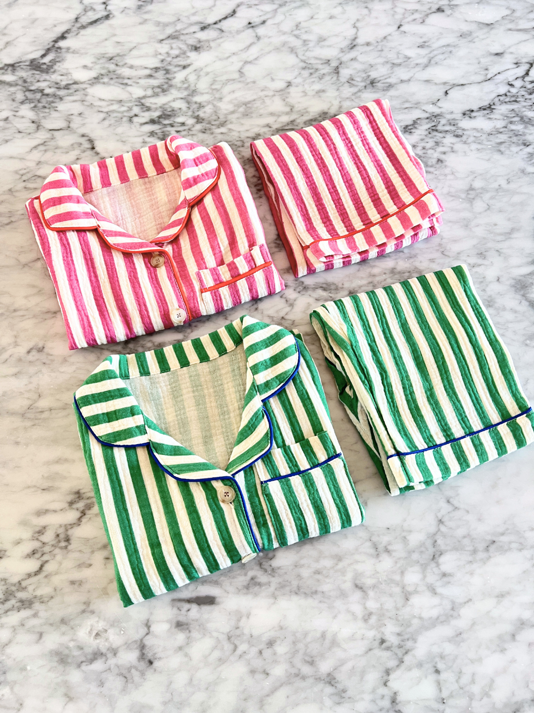 Pink Stripe | On a marble surface lie two sets of folded MOVIE NIGHT SET, one pink and white striped, the other green and white. Made from breathable cotton muslin, each set offers both comfort and style.