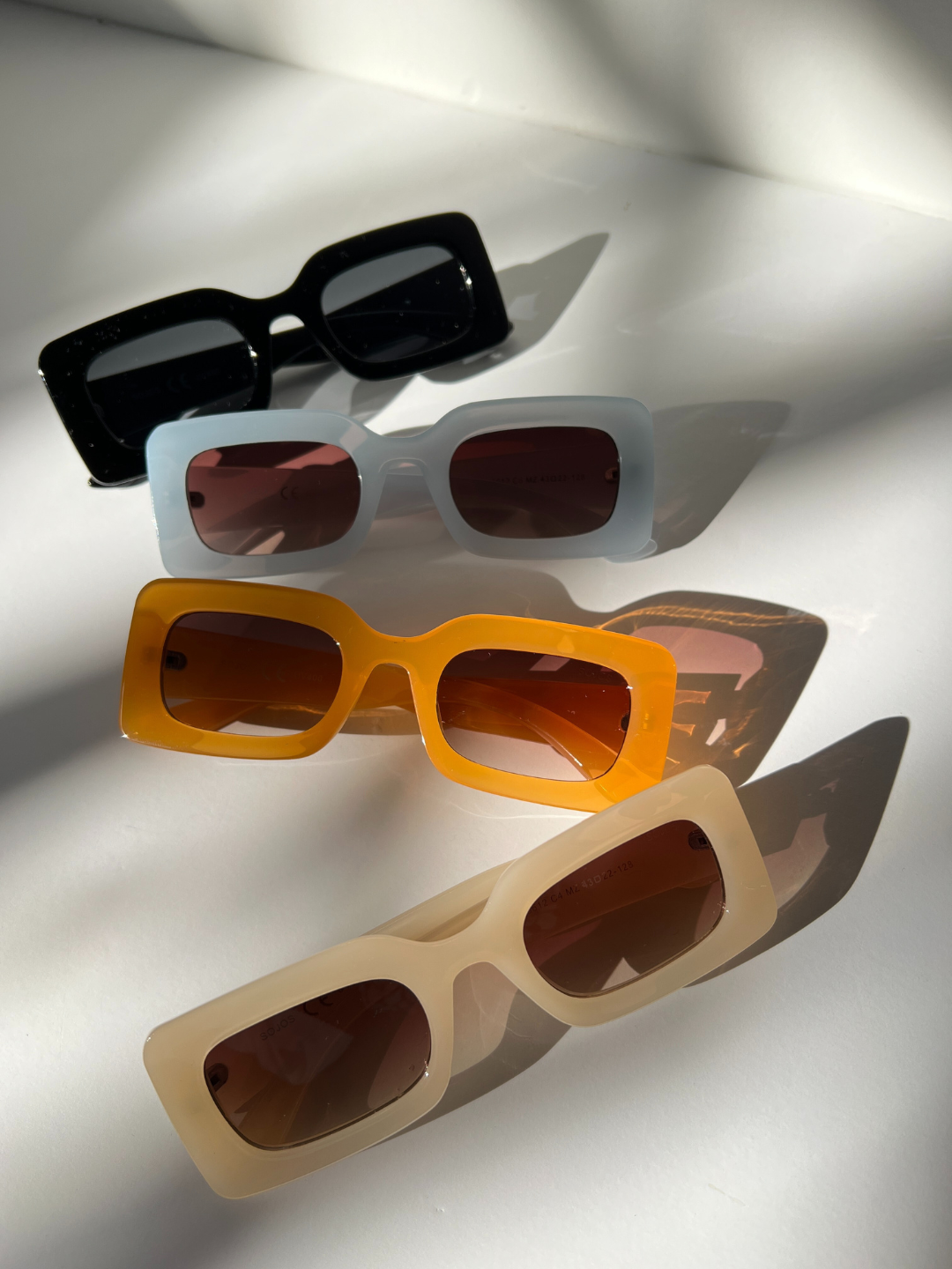 Group of kids rectangle sunglasses in black, blue, orange and cream, arranged on a white background.