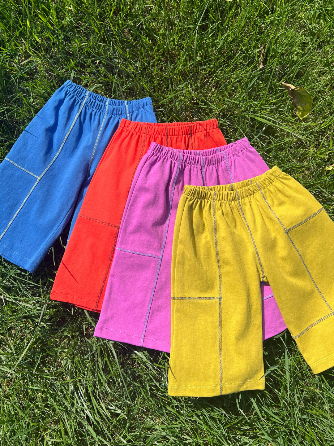 Magenta | Four pairs of colorful shorts (blue, red, pink, yellow) on grass.