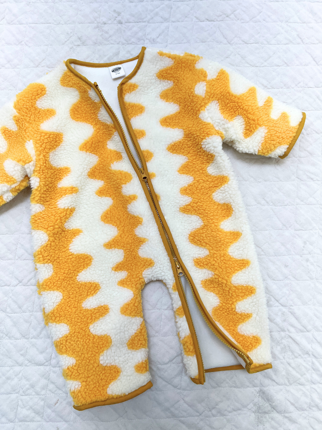 The WAVELENGTH SHERPA FLEECE STROLLER SUIT features yellow and white wavy zigzag stripes, a diagonal neck-to-leg zipper, and cozy sherpa fleece—perfect as a winter layer or stroller suit for your baby.