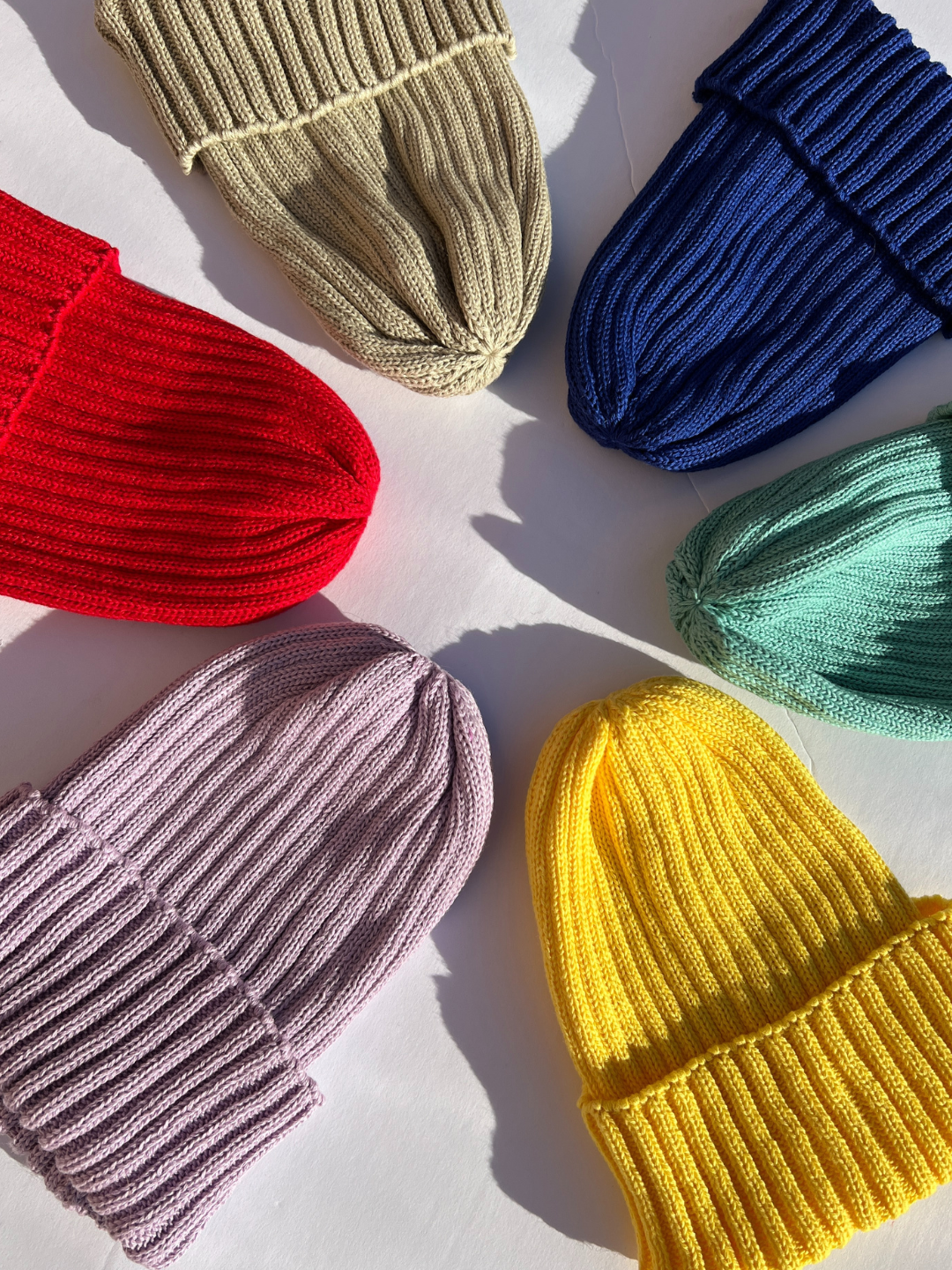 Group of lilac, red, khaki, blue, mint and yellow baby beanies on a white background.