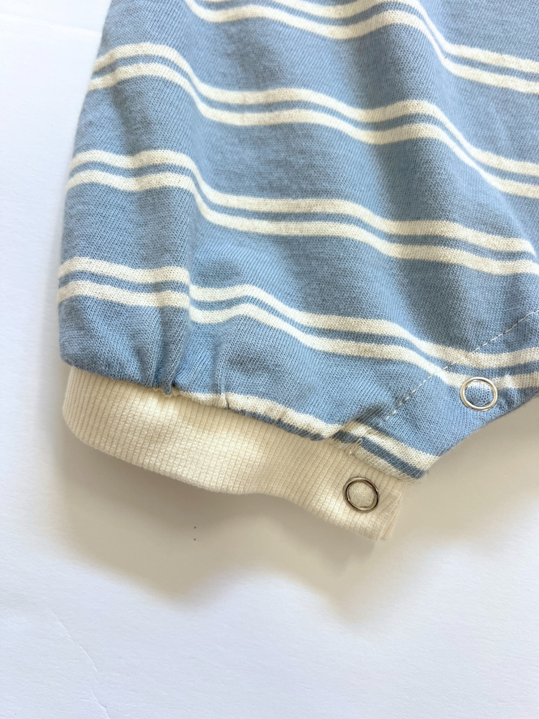 Close-up of the leg cuff of the SLOUCHY STRIPE ROMPER—a blue and white striped cotton jersey shortie with white ribbed trim and metal snaps. Perfect for your little one from a trusted Korean baby brand.