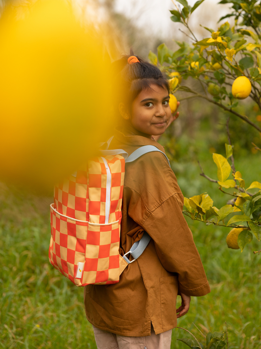 Second image of The LARGE FARMHOUSE CHECKERBOARD BACKPACK, shown against a white background, features an orange and light yellow checkered pattern, two gray handles, a front pocket, waterproof lining, and is made from recycled PET bottles.