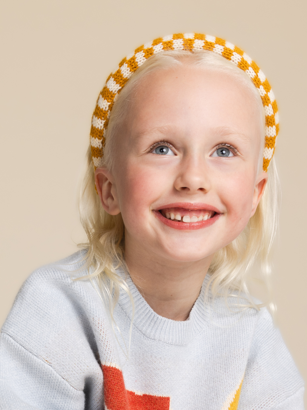 A child is wearing the ochre check headband