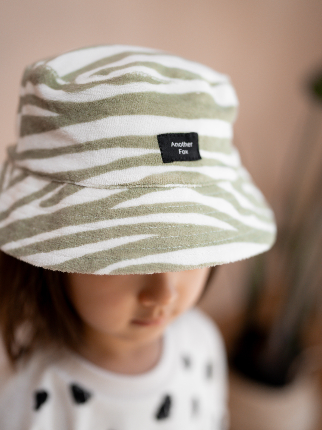 A zoomed in front view of the terry cloth hat on a child. Zebra print in a very light green and a gray-green.