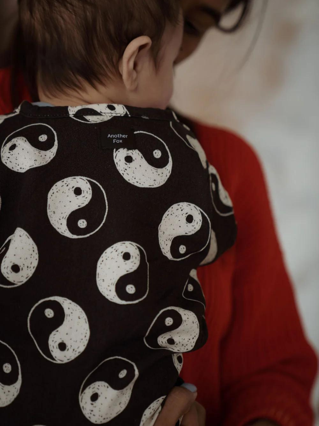 A zoomed in back view of the roomy jumpsuit on a child. Black with a yin and yang pattern all over. Front snap button closure.