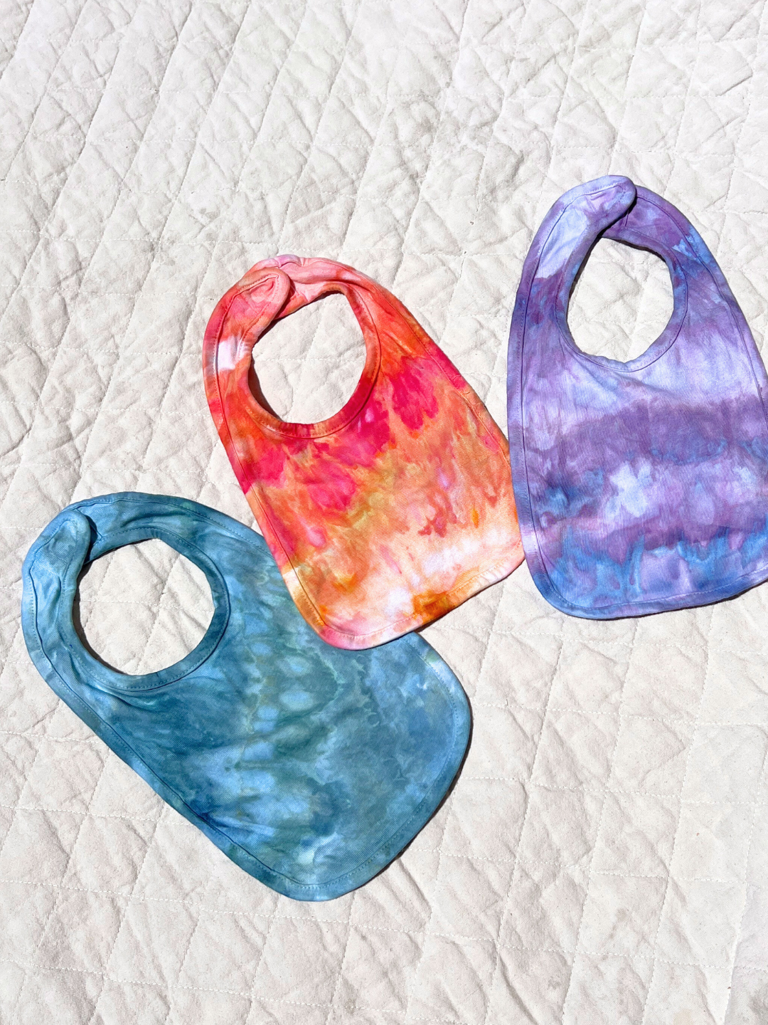 Three bibs in all three color ways are laid flat on a quilt.