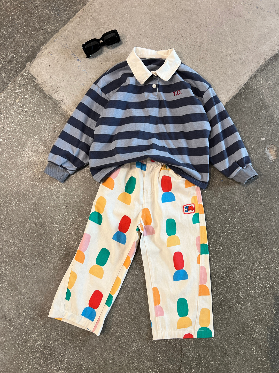 Blue | Children's outfit laid out on a concrete floor: trendy Korean kids brand's RUGBY LONGSLEEVE—gray and blue striped shirt with a white collar, paired with colorful patterned pants, and accessorized with black sunglasses.