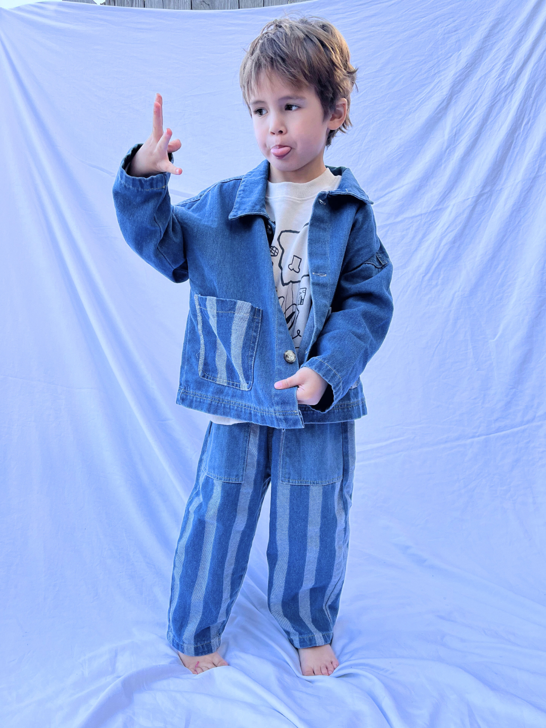 A child wearing a blue denim jacket and the Stripe Double Trouble Jeans with an elasticated waist stands on a white backdrop.