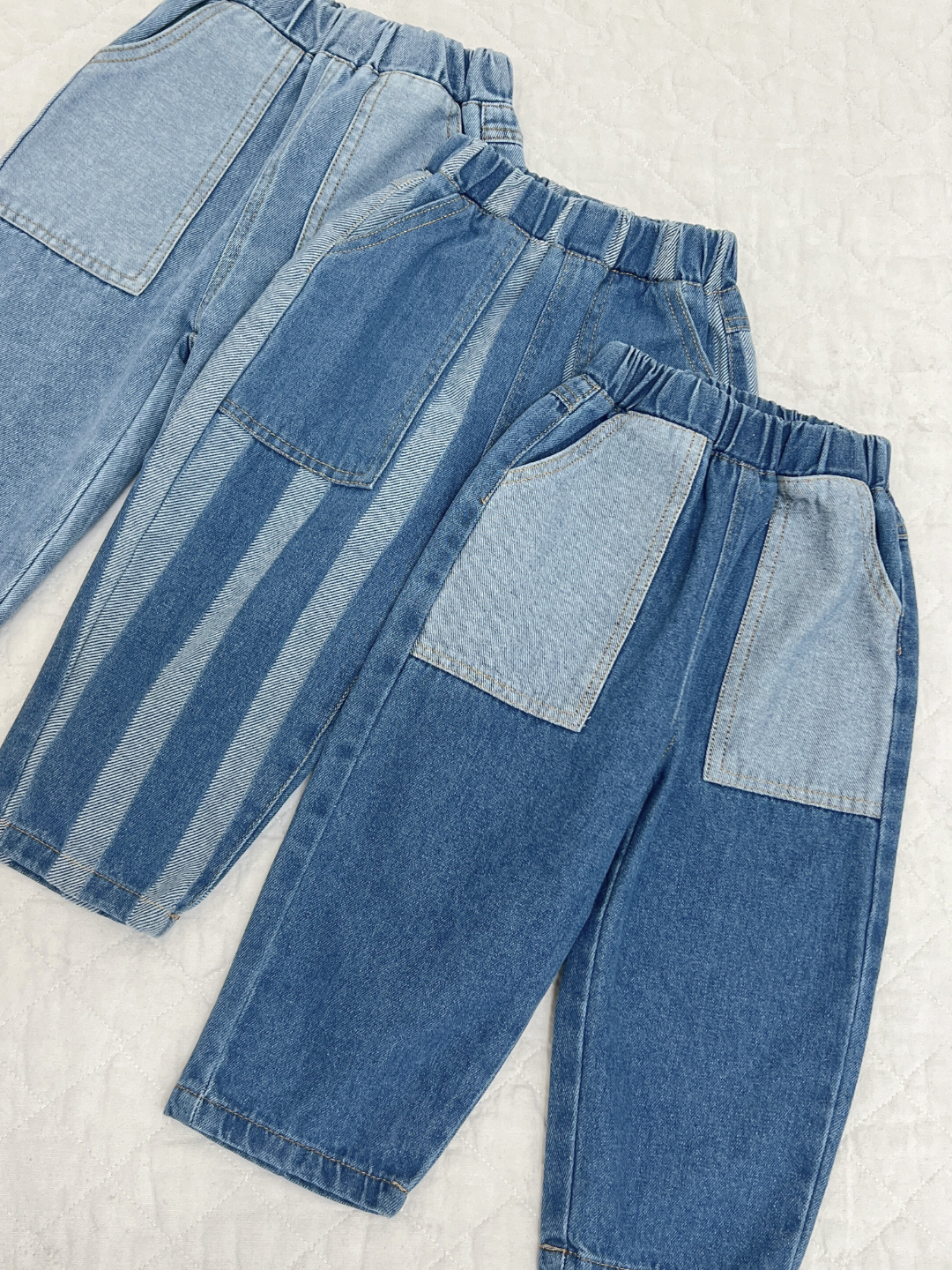 Double Trouble Jeans in Medium Wash, dark wash, and striped on a quilt. The three blue jeans have patch pockets.