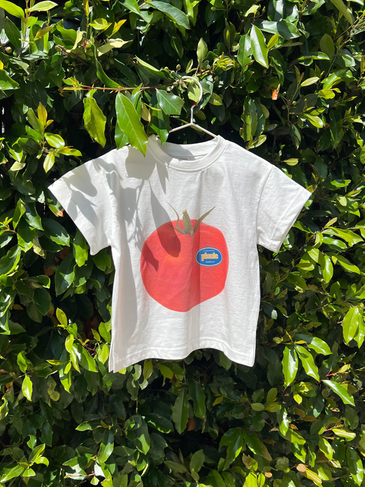 Second image of Tomato | PICNIC TEE in Tomato: an oversized white cotton t-shirt from a Korean kids brand, featuring a bold tomato graphic with a blue sticker label on the front, shown against a plain background.