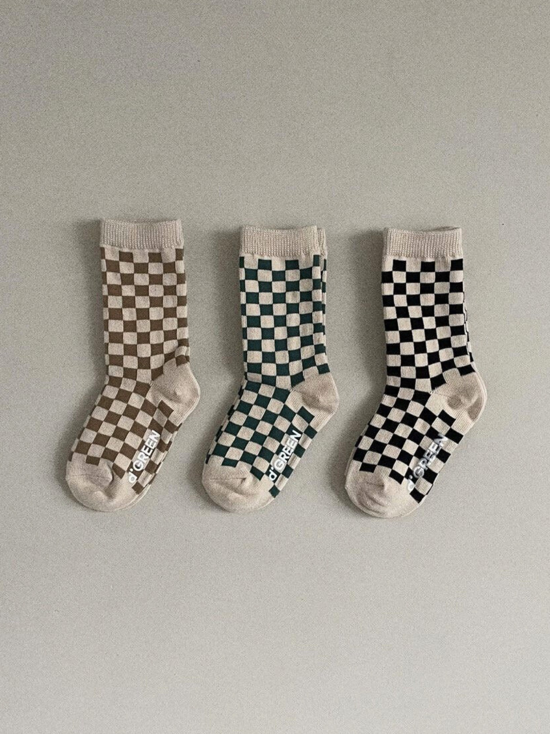 Set of three pairs of kids' checkerboard socks, in light brown, forest green, and black on an ecru background