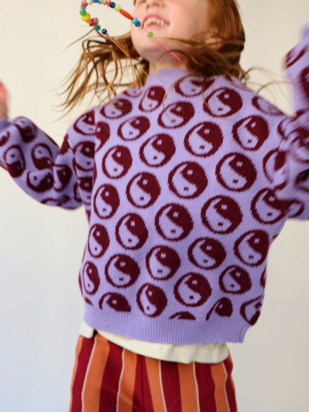 Happy child dancing in a violet kids' sweater printed with dark red yin and yang circles
