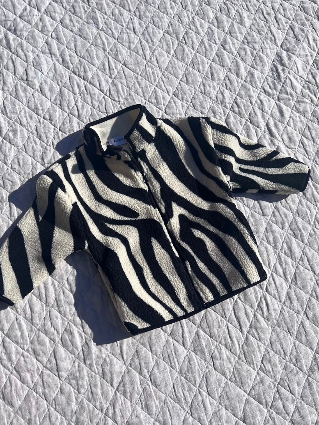 Kids fleece jacket in a black and cream tiger stripe pattern, laid down on a white quilt.