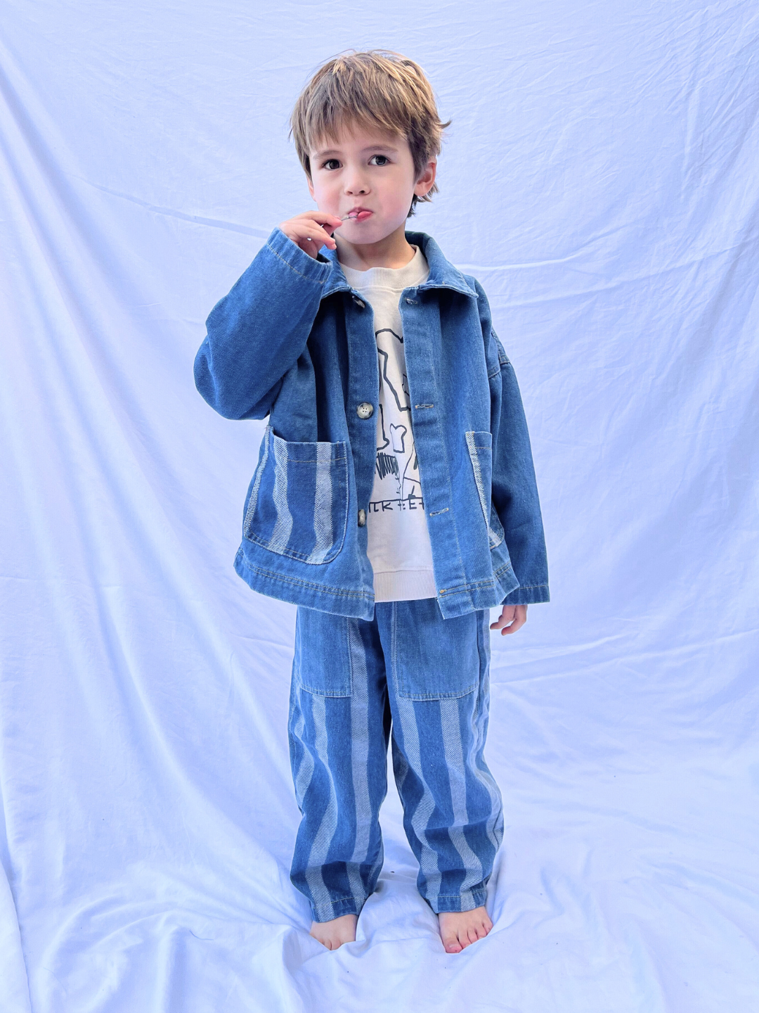 Medium Wash | A child wearing a blue denim jacket and the Stripe Double Trouble Jeans with an elasticated waist stands on a white backdrop.